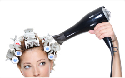 Model with a blow-dryer and hair in curlers.